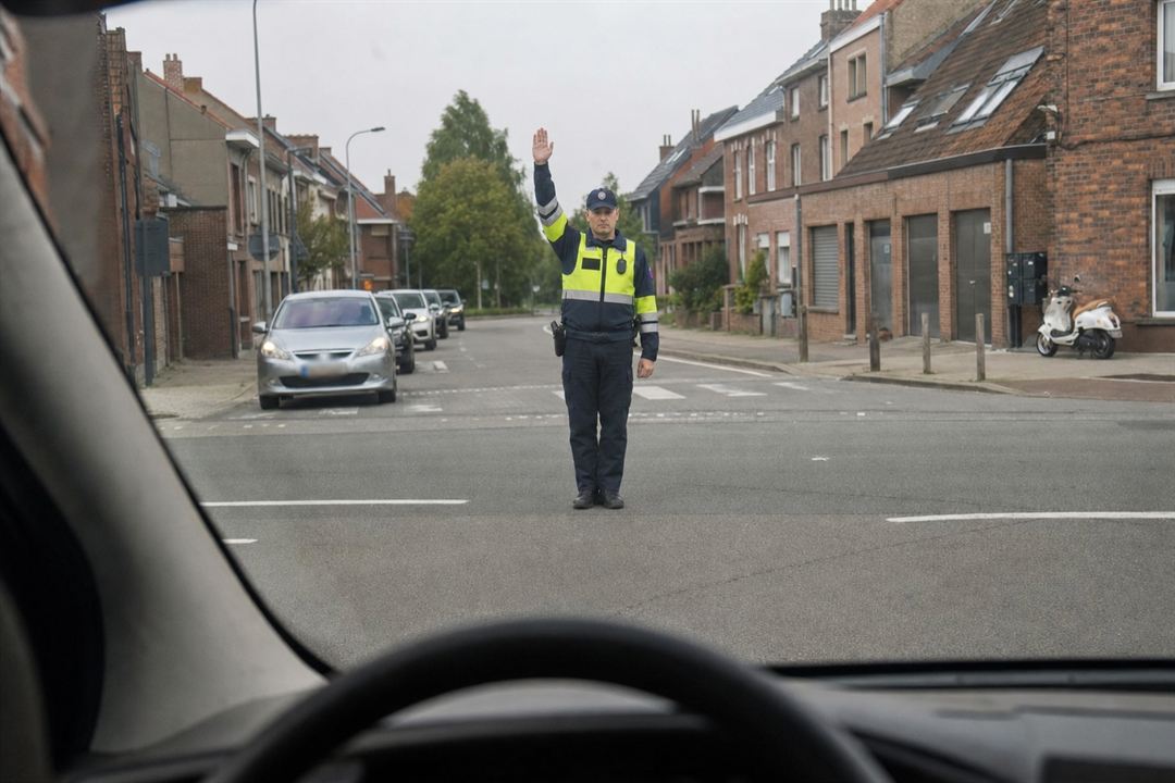 Agent belge au centre du carrefour, un bras levé verticalement, vu à travers le pare-brise