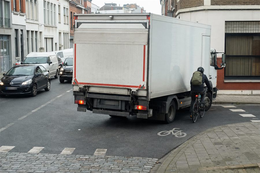 Cycliste longeant le flanc droit d'un camion arrêté au carrefour, invisible pour le chauffeur