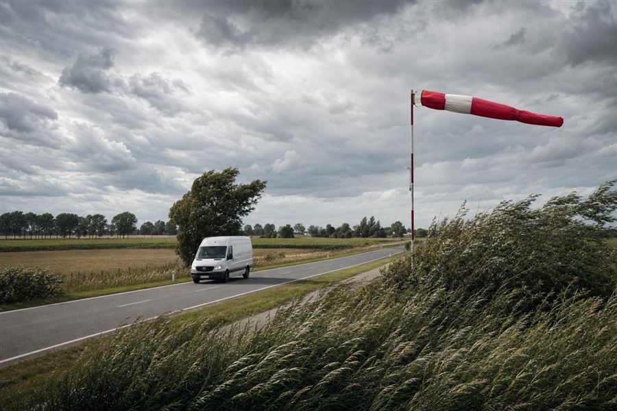 Camionnette roulant par vent violent, manche à air tendue et arbres courbés