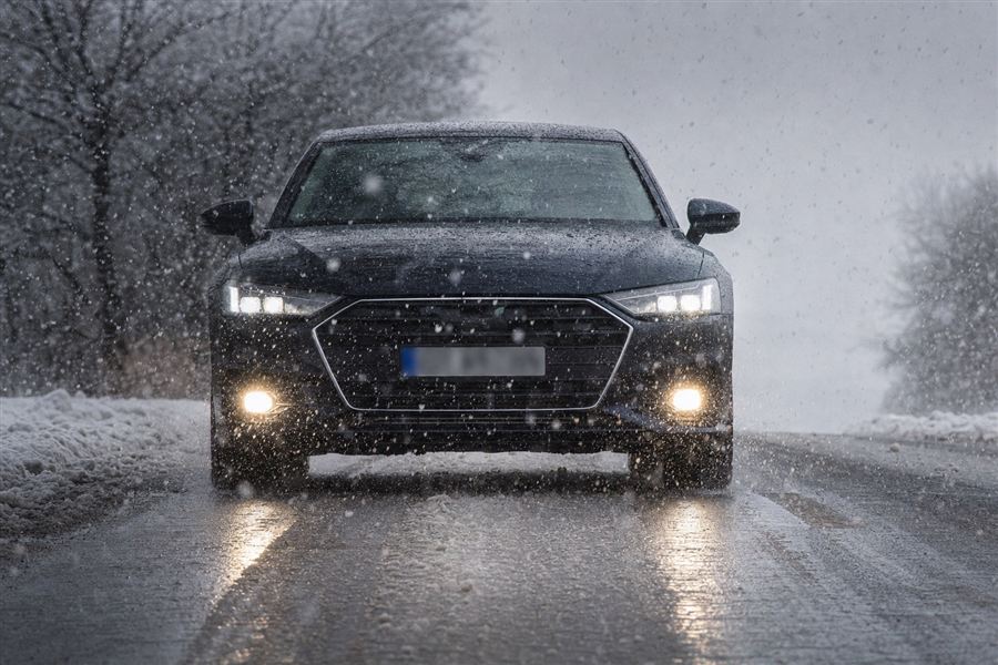 Voiture vue de face, feux allumés sous la neige et la pluie mêlées