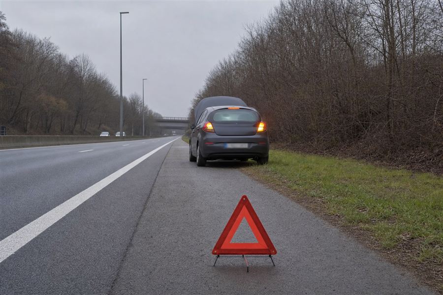 Voiture en panne capot ouvert, signalée par un triangle de danger, dépassée par une autre voiture