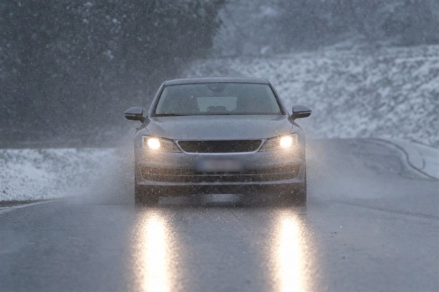 Voiture roulant feux allumés sous la neige et la pluie mêlées