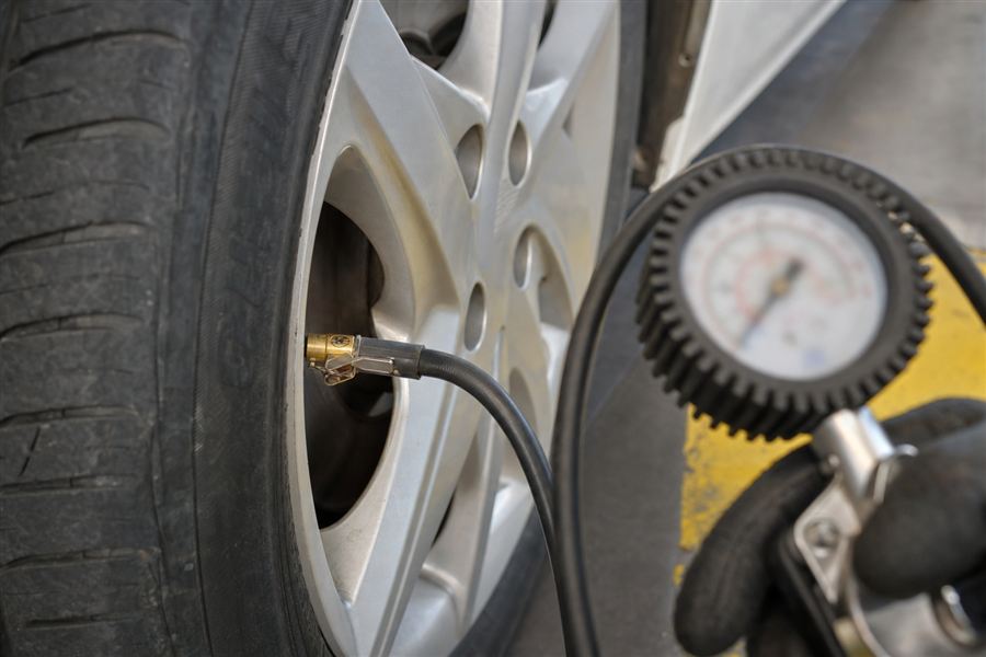 Conducteur qui vérifie la pression des pneus et le moteur de sa voiture avant de prendre la route